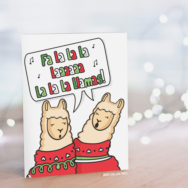 A white card with two Llamas wearing ugly Christmas sweaters singing "Fa la la la la laaaaaa la la la llamas!"