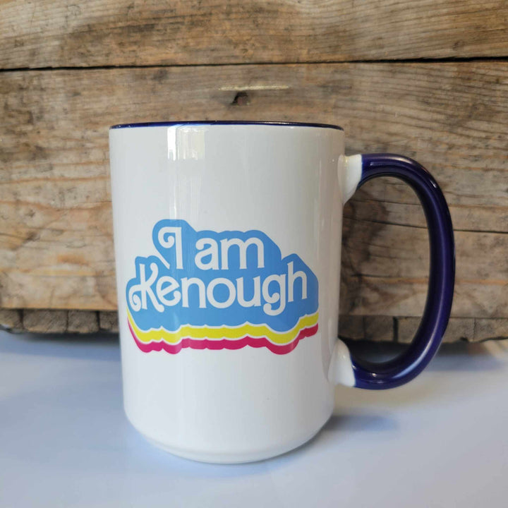 15oz ceramic mug with "I am Kenough" written in white Barbie Lettering with a blue, yellow, and pink border. The mug is dishwasher safe but handwash is recommended.