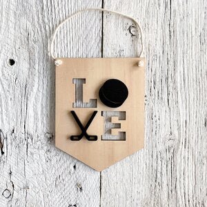 Laser engraved 3D wall flag that says "LOVE" with a hockey puck as the letter "O" and crossed hockey sticks for the letter "V".