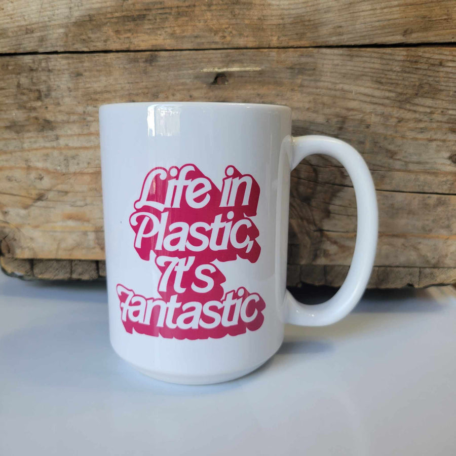 15oz ceramic mug that says "Life in Plastic, It's Fantastic" in pink barbie font. The mug is dishwasher safe but handwash is recommended