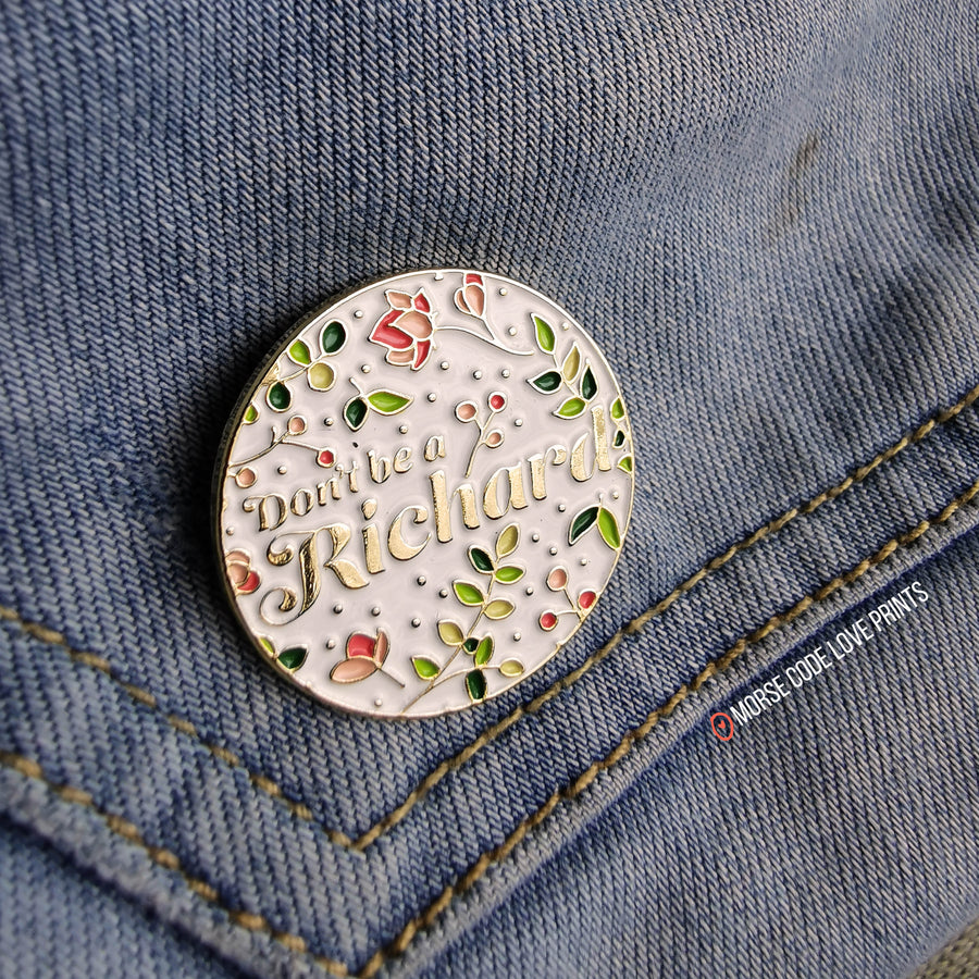 This round floral pins and says "don't be a Richard", it measures 1 1/4" along the longest edge.
