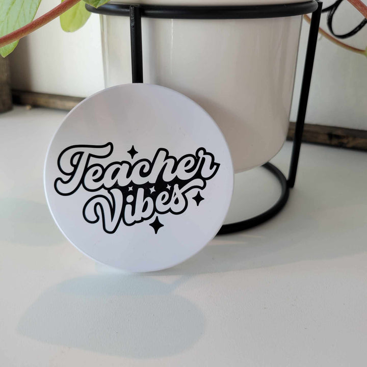 Smooth matte finish ceramic coaster that says "Teacher Vibes" in white bubble letters with a black outline. Bumper dots on the bottom.