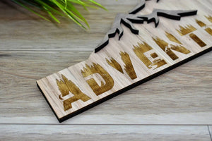 Great looking wall decor sign that reminds us adventure is always waiting to happen. Engraved in beautiful red oak with a special "wild and nature" artistic font, and raised mountains made of walnut. This sign can decorate any room. Mounting holes are provided in the back for quick and easy installation.